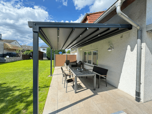 An der Hauswand montierte Aluminium-Pergola über einer Terrasse mit Esstisch