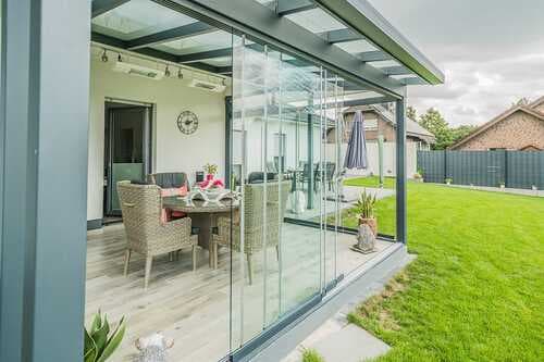 Geschlossener Anbau aus Aluminium mit rahmenlosen Glasschiebeelementen, im Innenraum ein gedeckter Esstisch